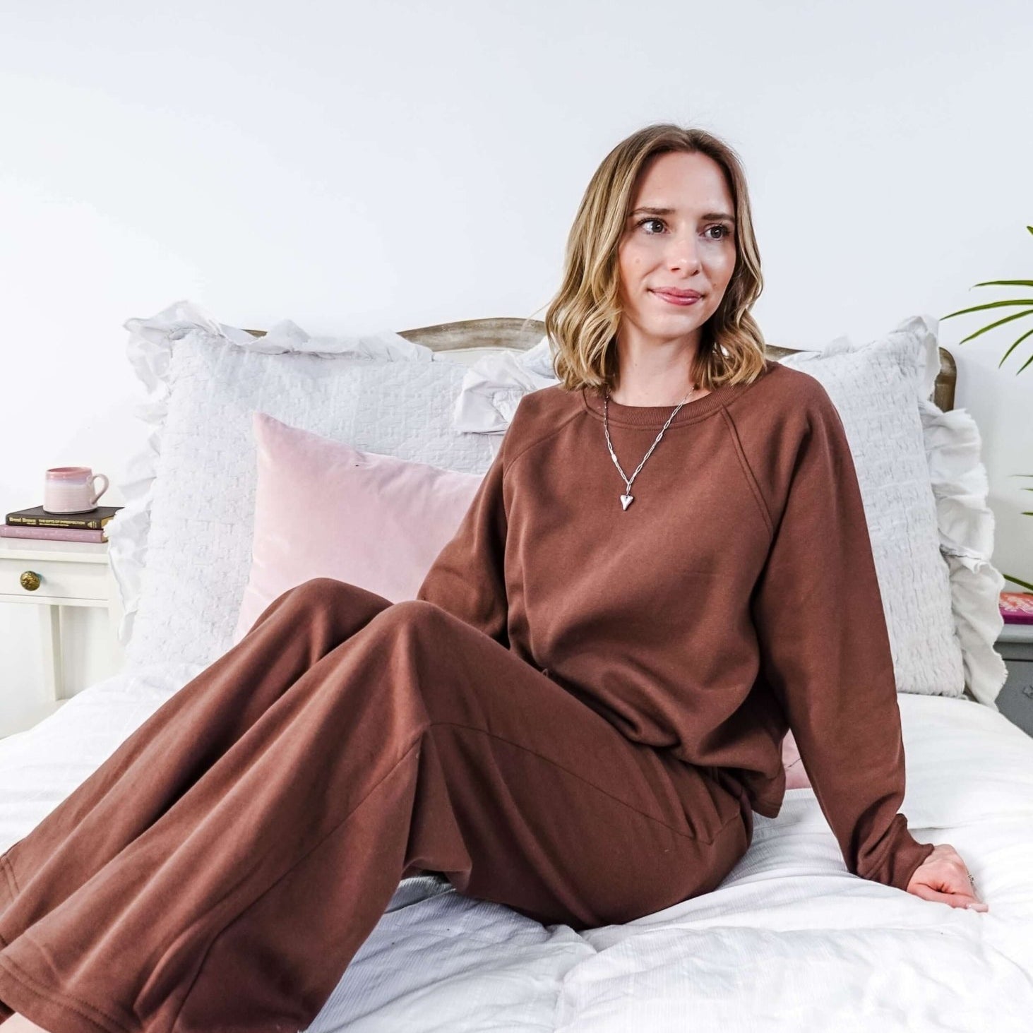 Woman in brown lounge set sitting on a bed with white bedding