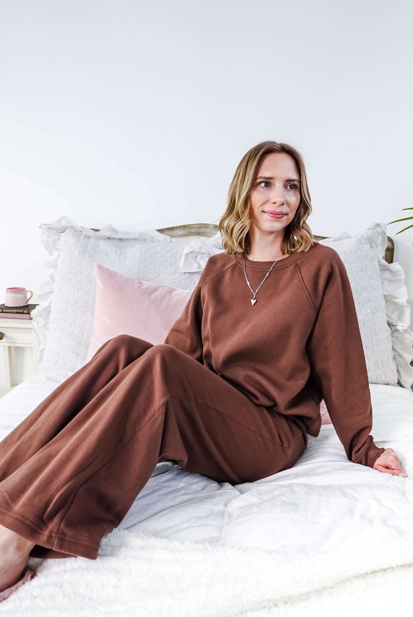 Woman in brown lounge set sitting on a bed with white bedding