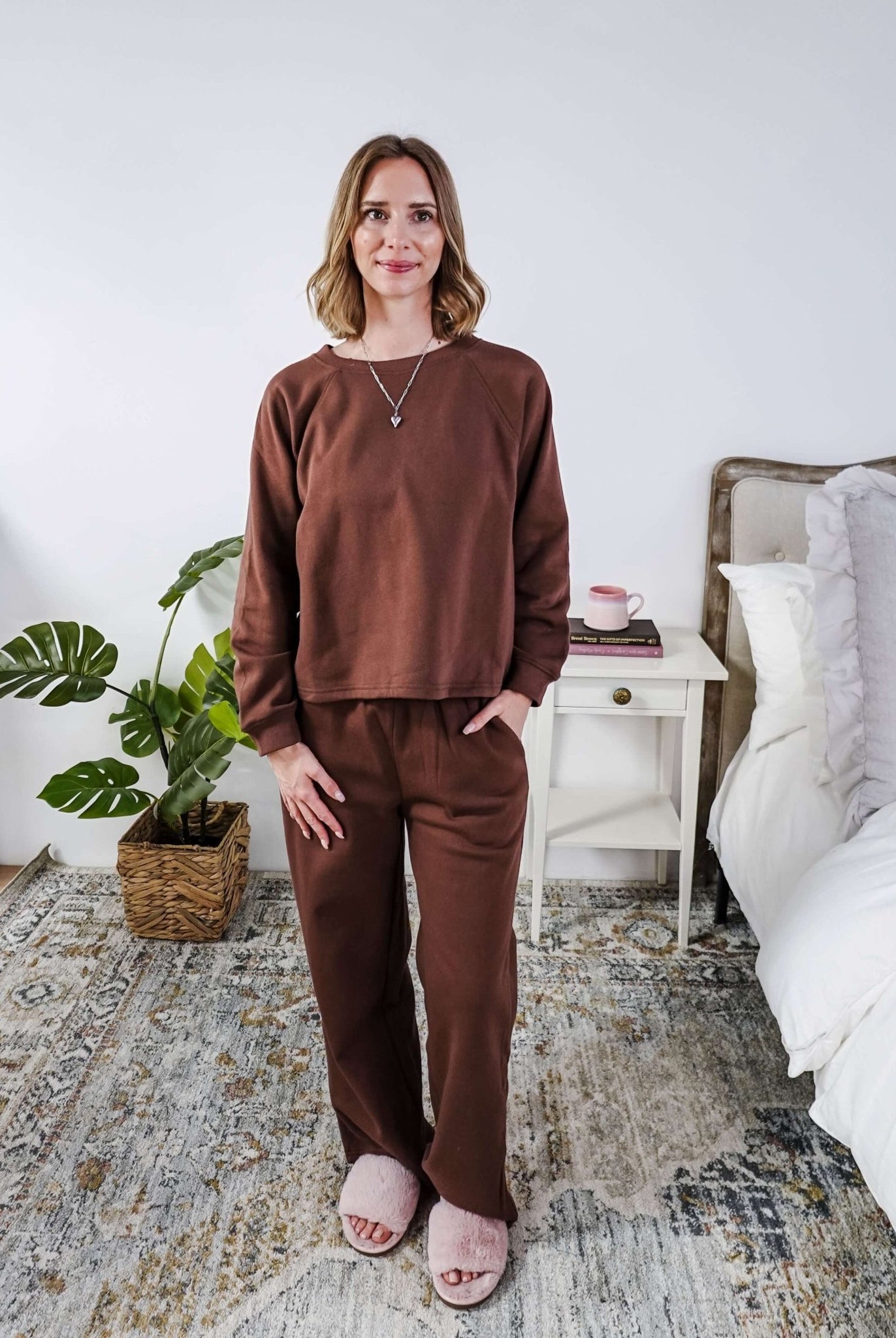 Woman wearing a brown lounge outfit standing in a bedroom.