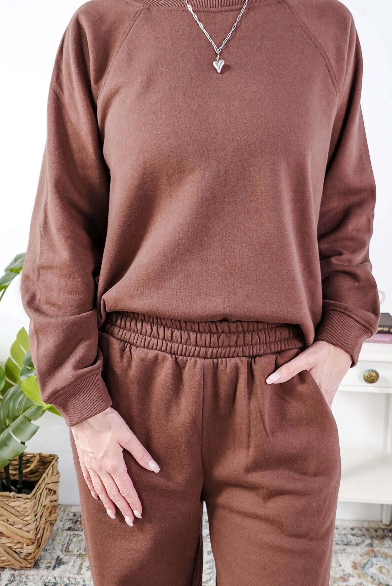 Person wearing a brown sweatshirt and sweat pants with elastic waistband and pants in a home setting.