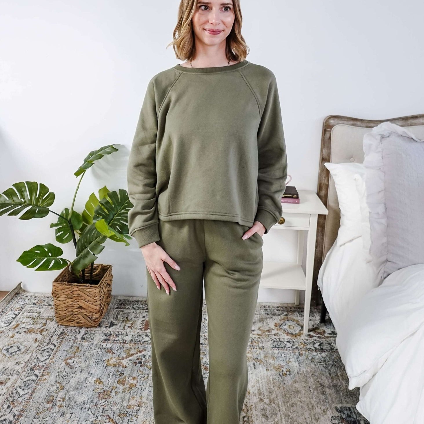 Woman wearing an olive green sweatset standing in a bedroom.