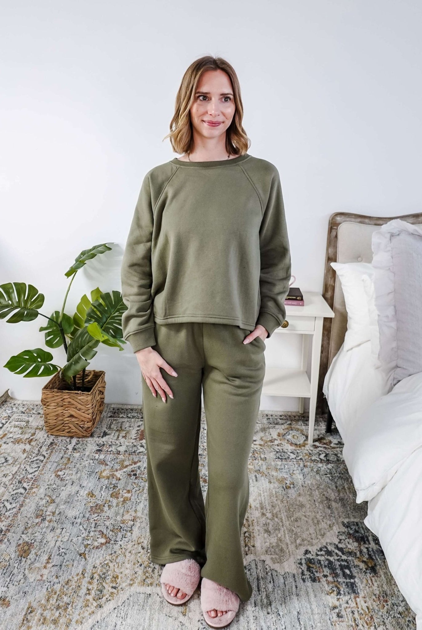 Woman wearing an olive green sweatset standing in a bedroom.