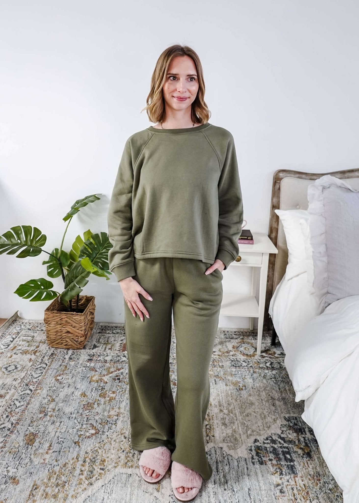Woman wearing an olive green sweatset standing in a bedroom.