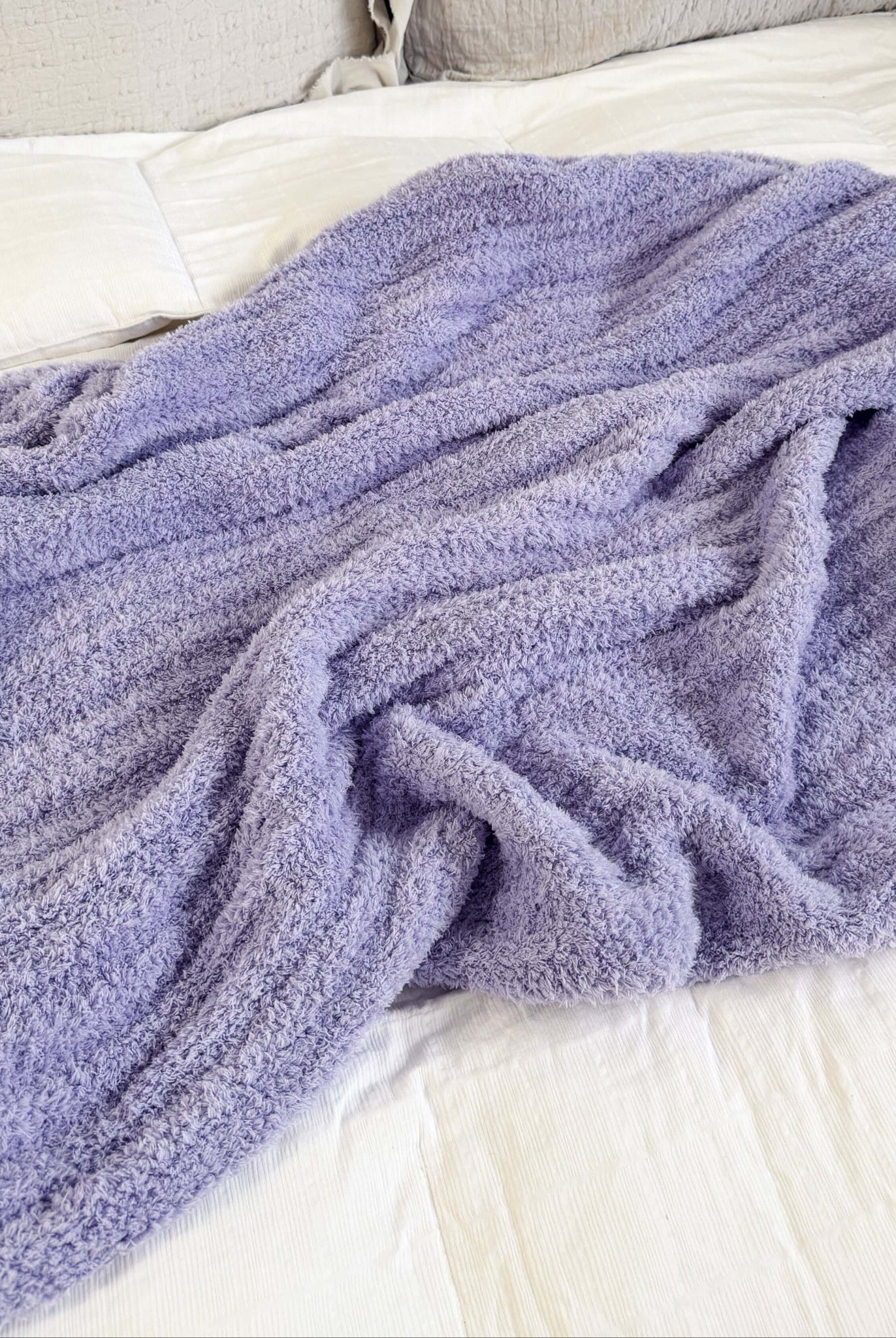 Purple blanket draped over a bed with beige pillows