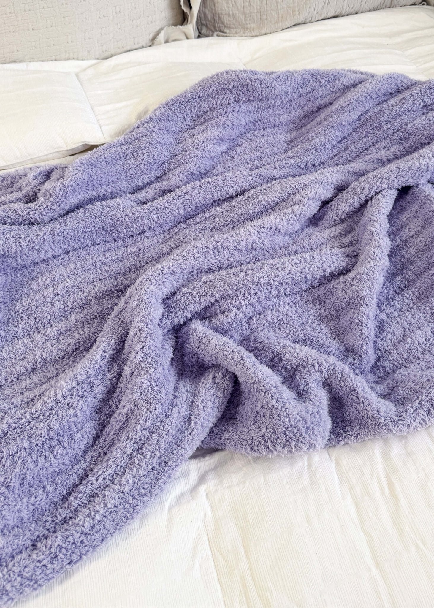 Purple blanket draped over a bed with beige pillows