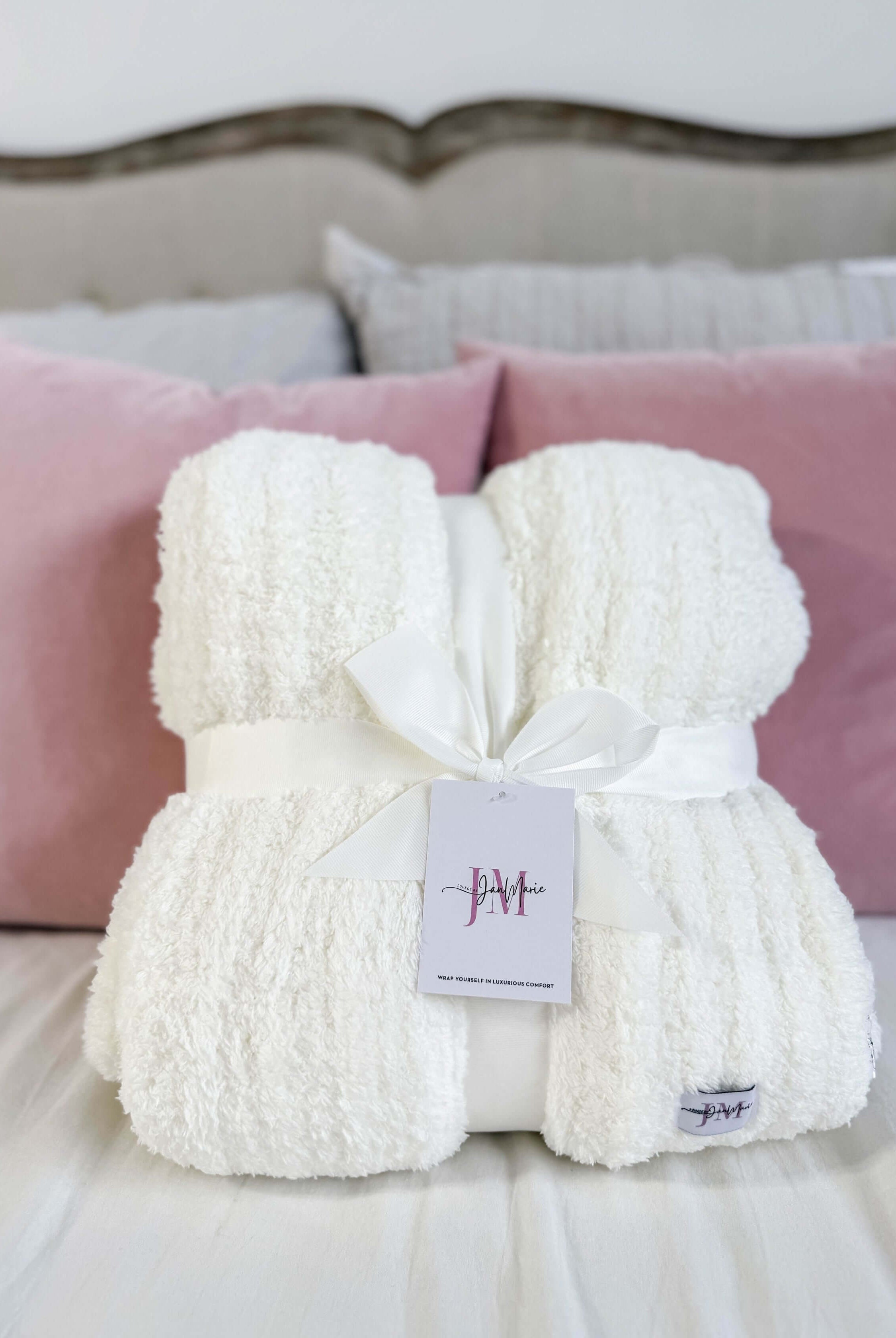 White fluffy blanket with a tag on a bed with pink pillows