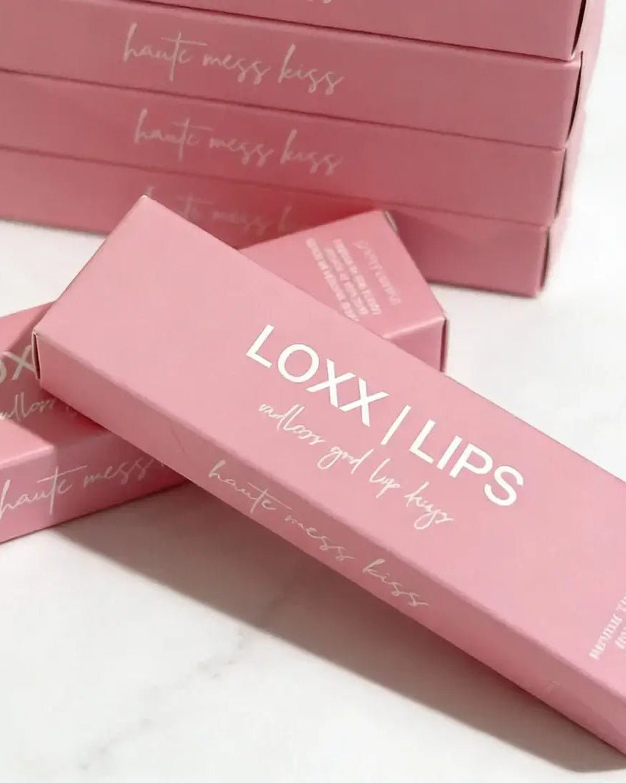 LOXX LIPS Peptide Lip Gloss Haute Mess Kiss Pink Tint packaging displayed on a marble surface.
