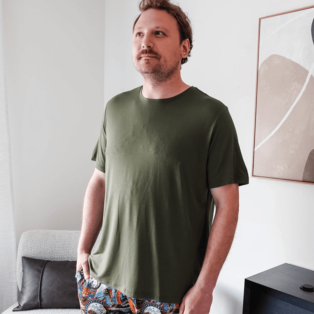 Man wearing the Olive Forest Unisex Short Sleeve Tee Bamboo with colorful patterned pants in a modern interior.