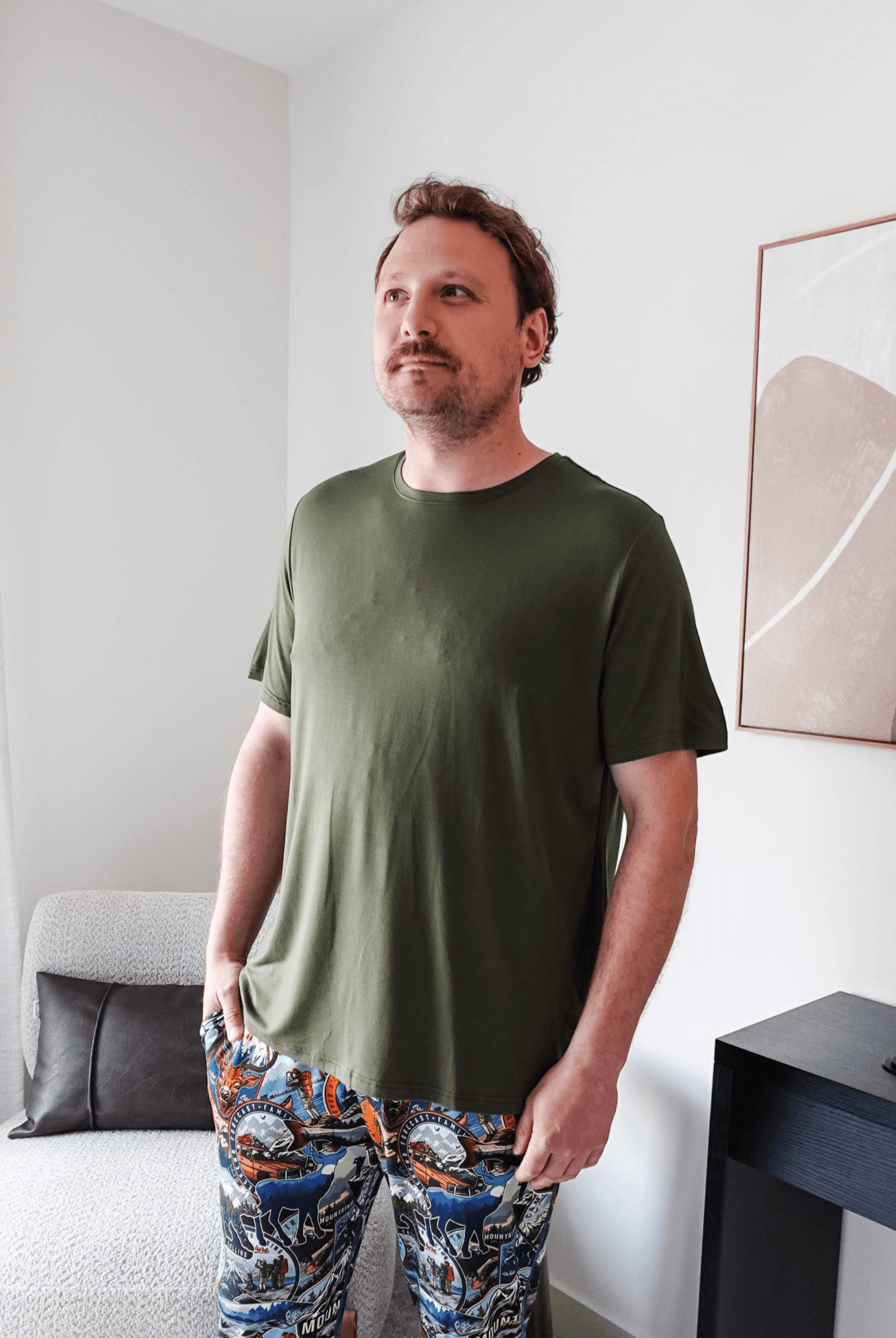Man wearing the Olive Forest Unisex Short Sleeve Tee Bamboo with colorful patterned pants in a modern interior.