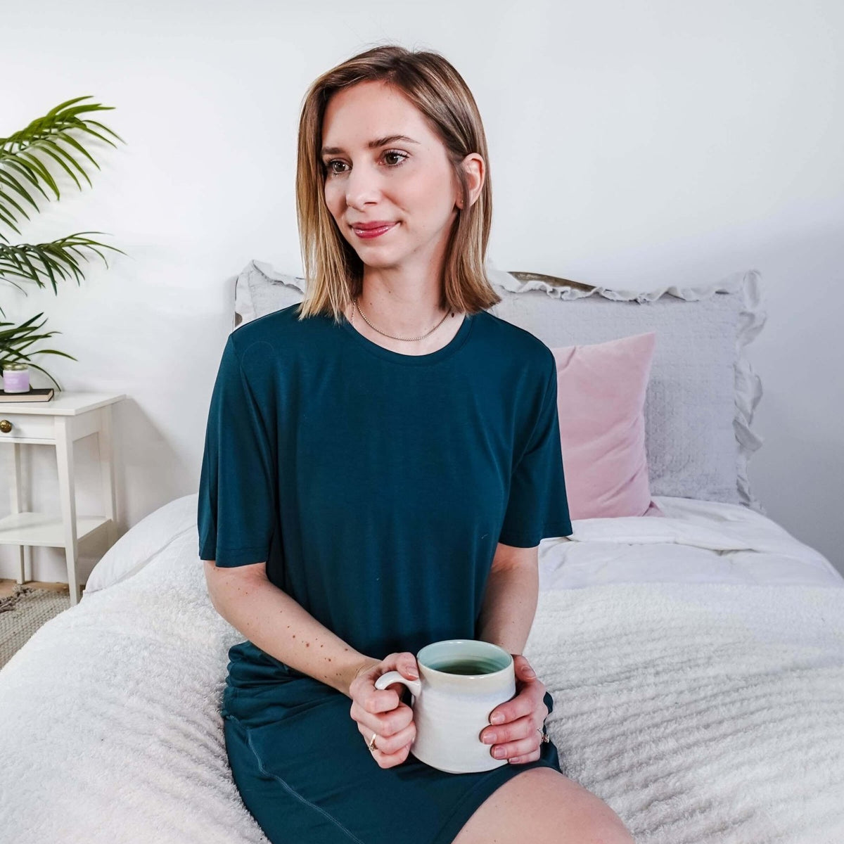 Woman wearing Midnight Teal Unisex Bamboo Sleep Shorts while holding a cup of tea in a cozy bedroom setting.