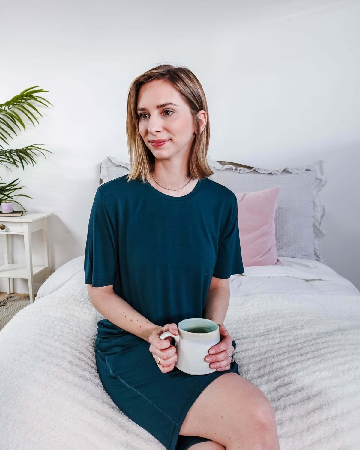 Woman wearing Midnight Teal Unisex Bamboo Sleep Shorts while holding a cup of tea in a cozy bedroom setting.