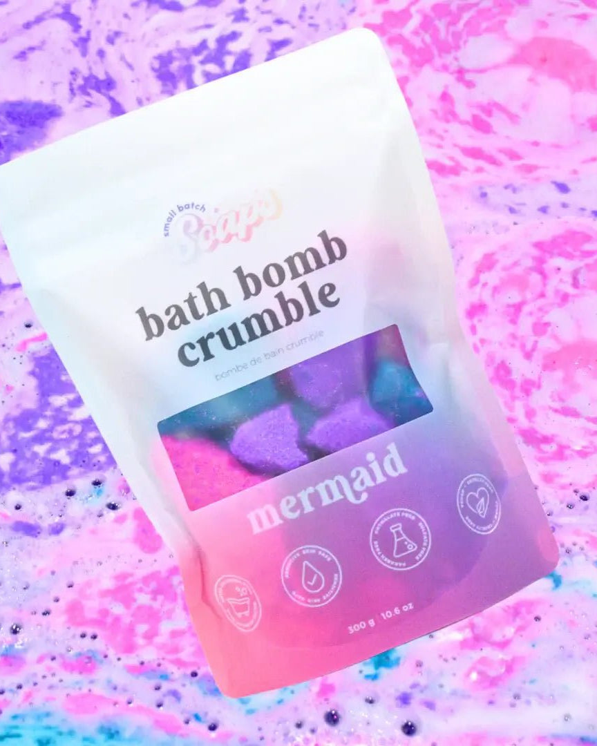 Mermaid Bath Bomb Crumble in a colorful package with fizzling bath water in the background.