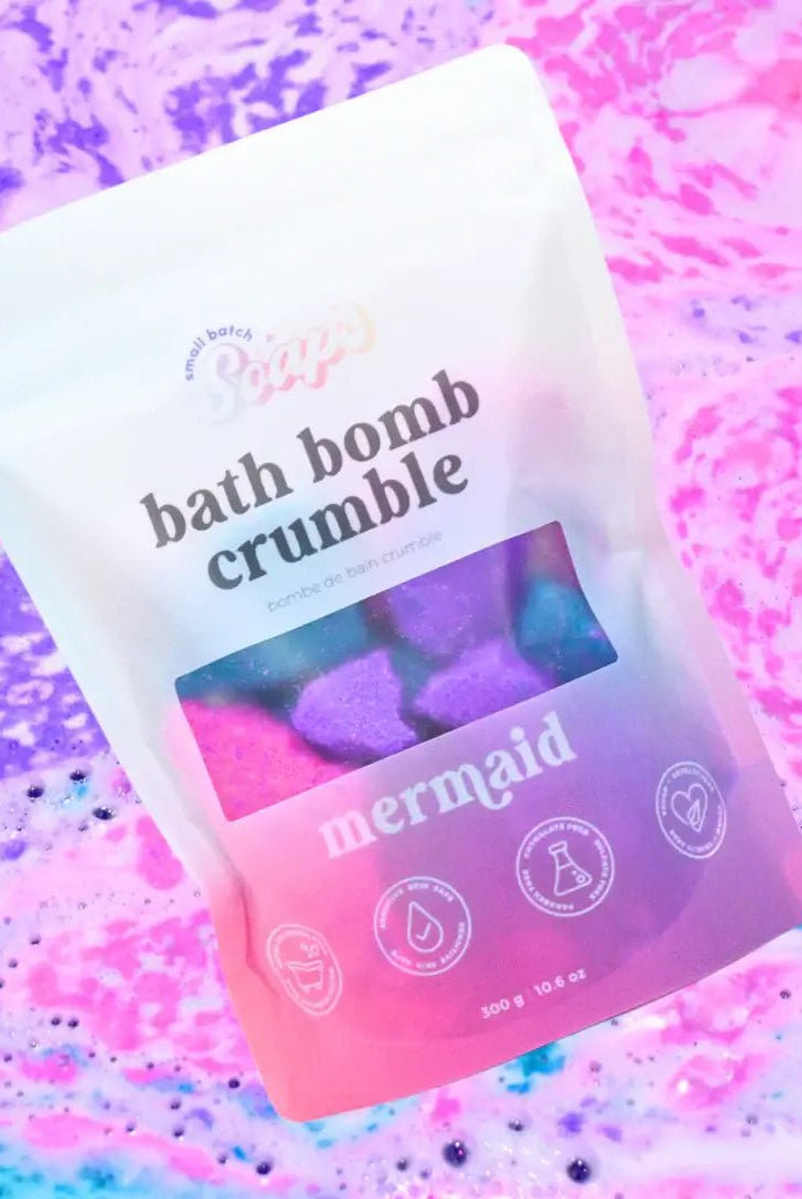 Mermaid Bath Bomb Crumble in a colorful package with fizzling bath water in the background.