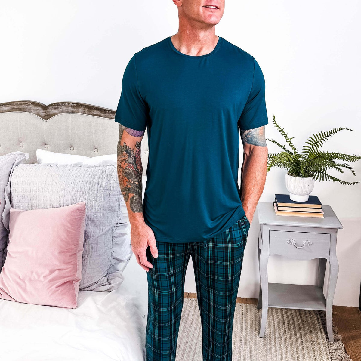 Model wearing Midnight Plaid Unisex Bamboo Joggers paired with a blue shirt in a cozy bedroom setting.