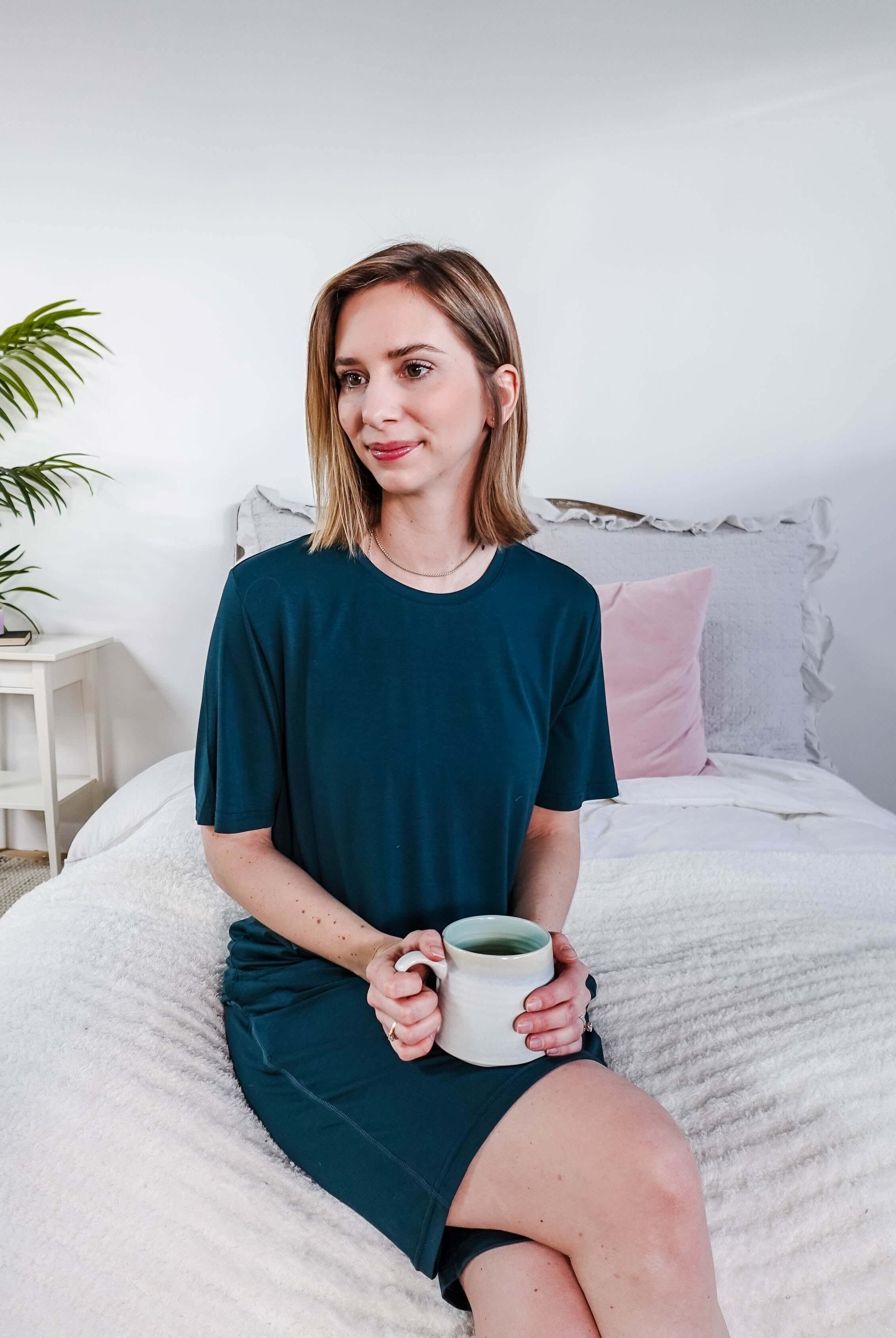 Woman wearing Midnight Teal Unisex Bamboo Sleep Shorts while holding a cup of tea in a cozy bedroom setting.