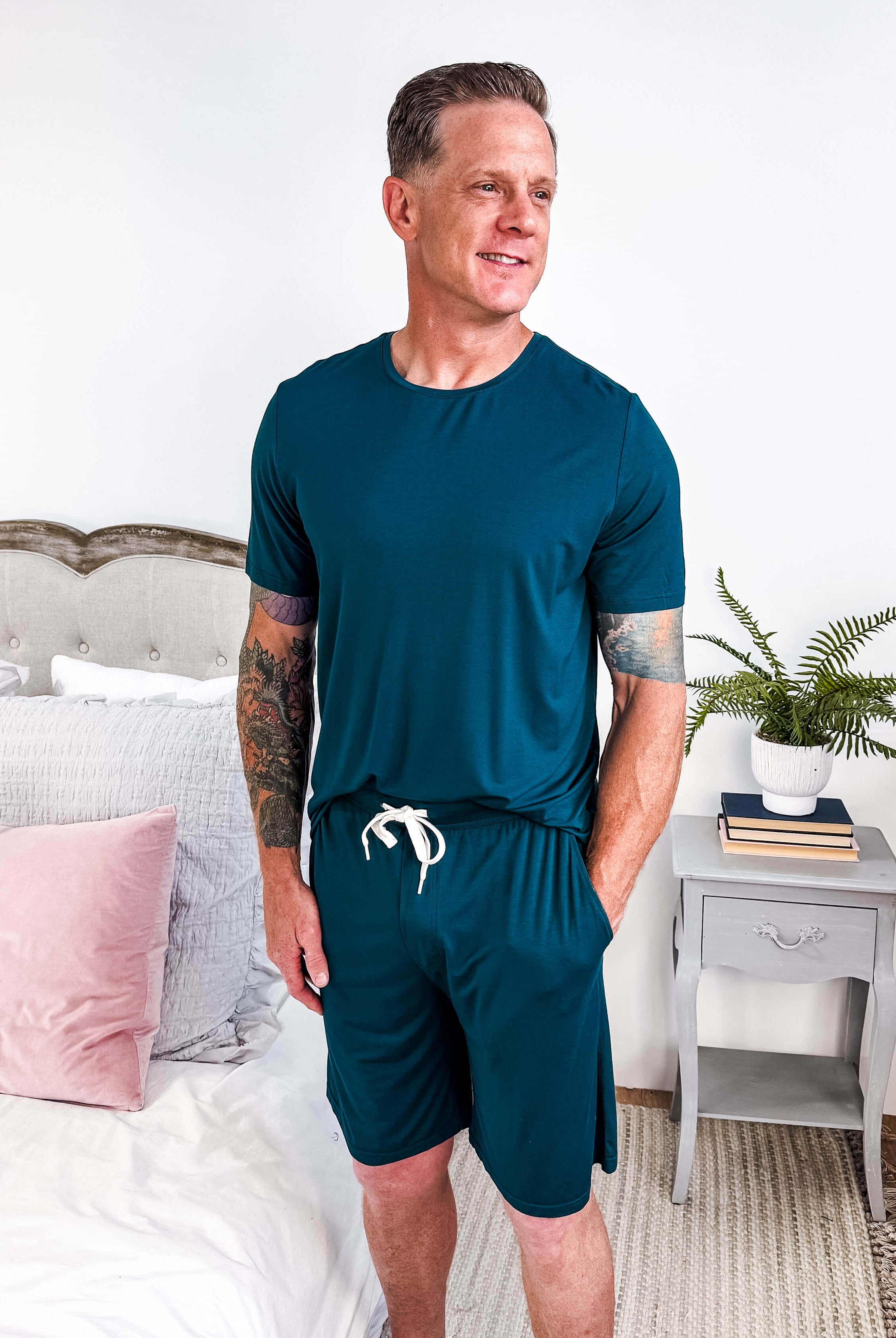 Midnight Teal Unisex Bamboo Sleep Shorts being modeled in a cozy bedroom setting with light decor.