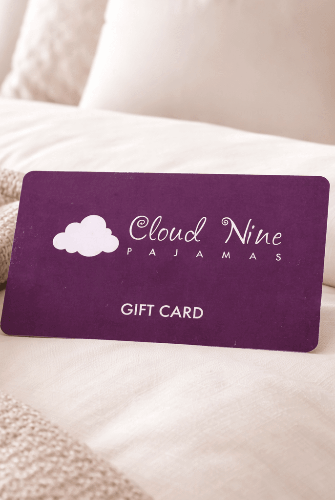 Purple 'Cloud Nine Pajamas' gift card on a bed with beige pillows and blanket.