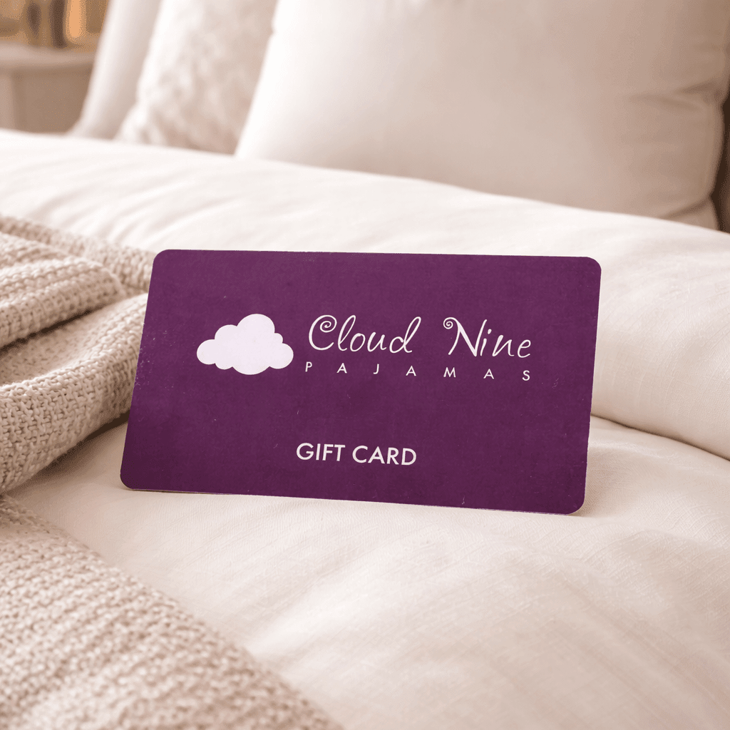 Purple 'Cloud Nine Pajamas' gift card on a bed with beige pillows and blanket.