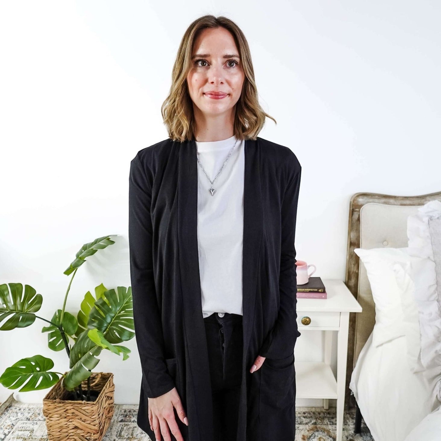 Woman in a black cardigan standing in a room with a plant and a bed in the background Scarlett Ellie Summer Open Lightweight Cardigan | Cloud Nine Pajamas