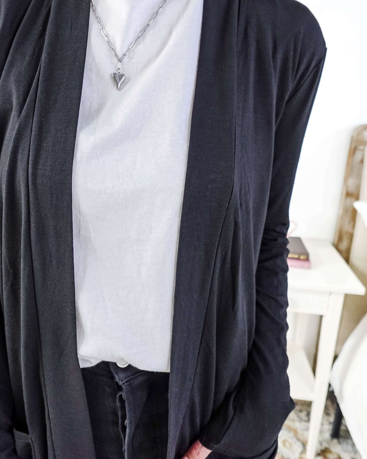 Woman in a black cardigan standing in a room with a plant and a bed in the background Scarlett Ellie Summer Open Lightweight Cardigan | Cloud Nine Pajamas