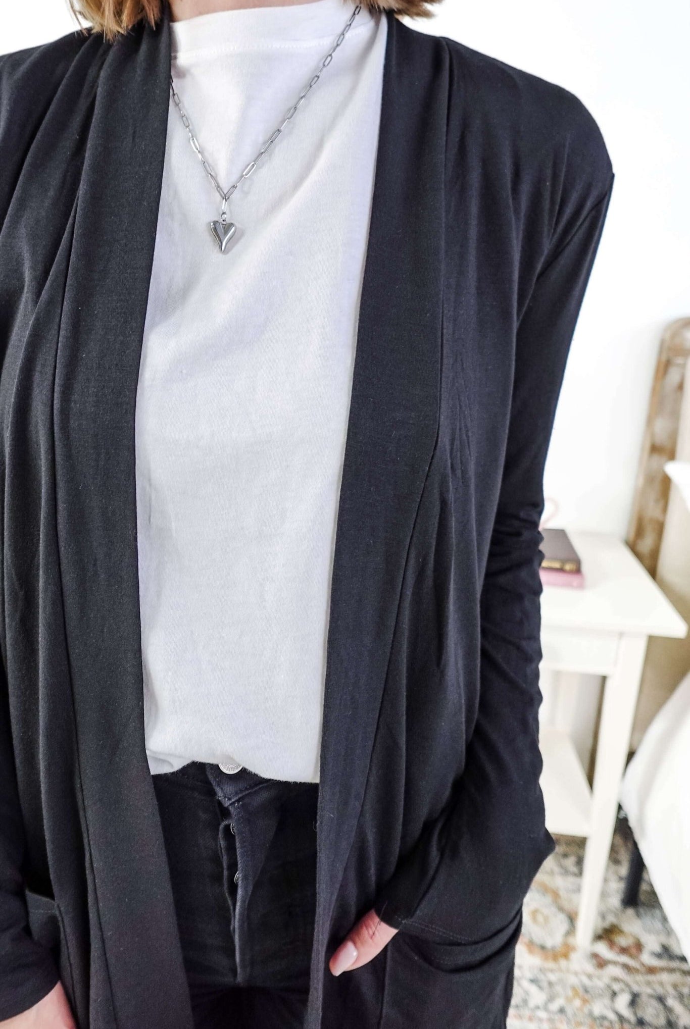 Woman in a black cardigan standing in a room with a plant and a bed in the background Scarlett Ellie Summer Open Lightweight Cardigan | Cloud Nine Pajamas