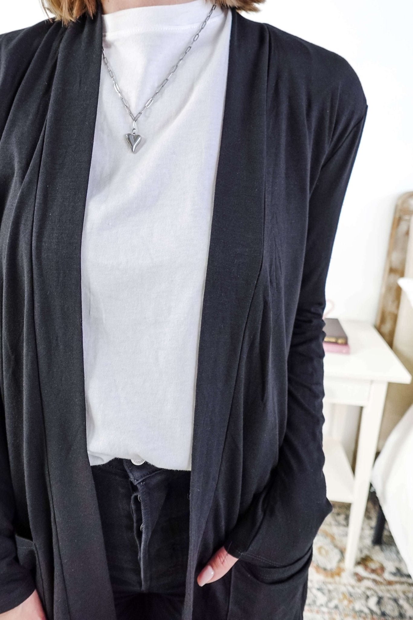 Woman in a black cardigan standing in a room with a plant and a bed in the background Scarlett Ellie Summer Open Lightweight Cardigan | Cloud Nine Pajamas