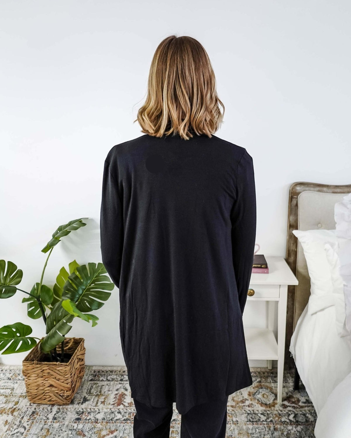 Woman in a black cardigan standing in a room with a plant and a bed in the background Scarlett Ellie Summer Open Lightweight Cardigan | Cloud Nine Pajamas
