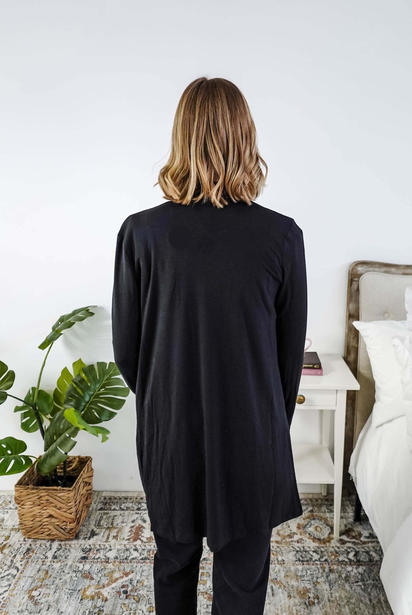 Woman in a black cardigan standing in a room with a plant and a bed in the background Scarlett Ellie Summer Open Lightweight Cardigan | Cloud Nine Pajamas