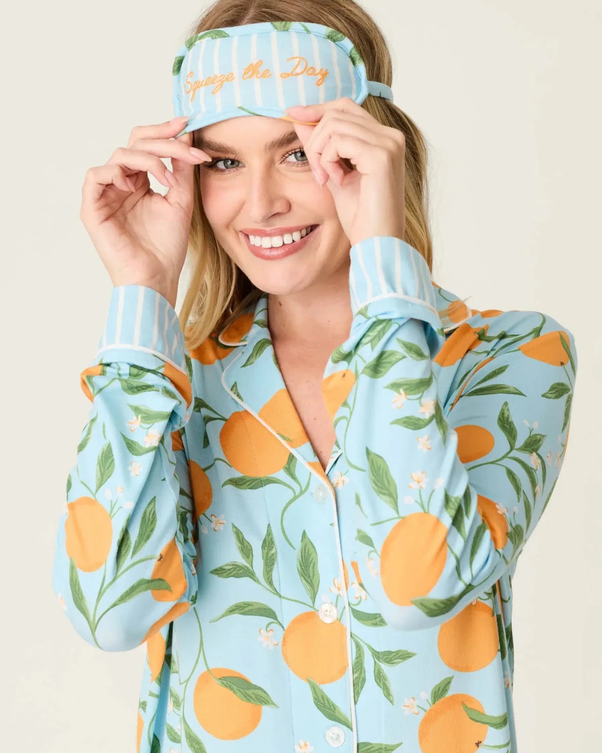 Model wearing PJ Salvage Citrus Dreams 3-Piece PJ Set featuring orange design with matching eye mask. Close up view of Eye mask and embroidery saying "Squeeze the Day"