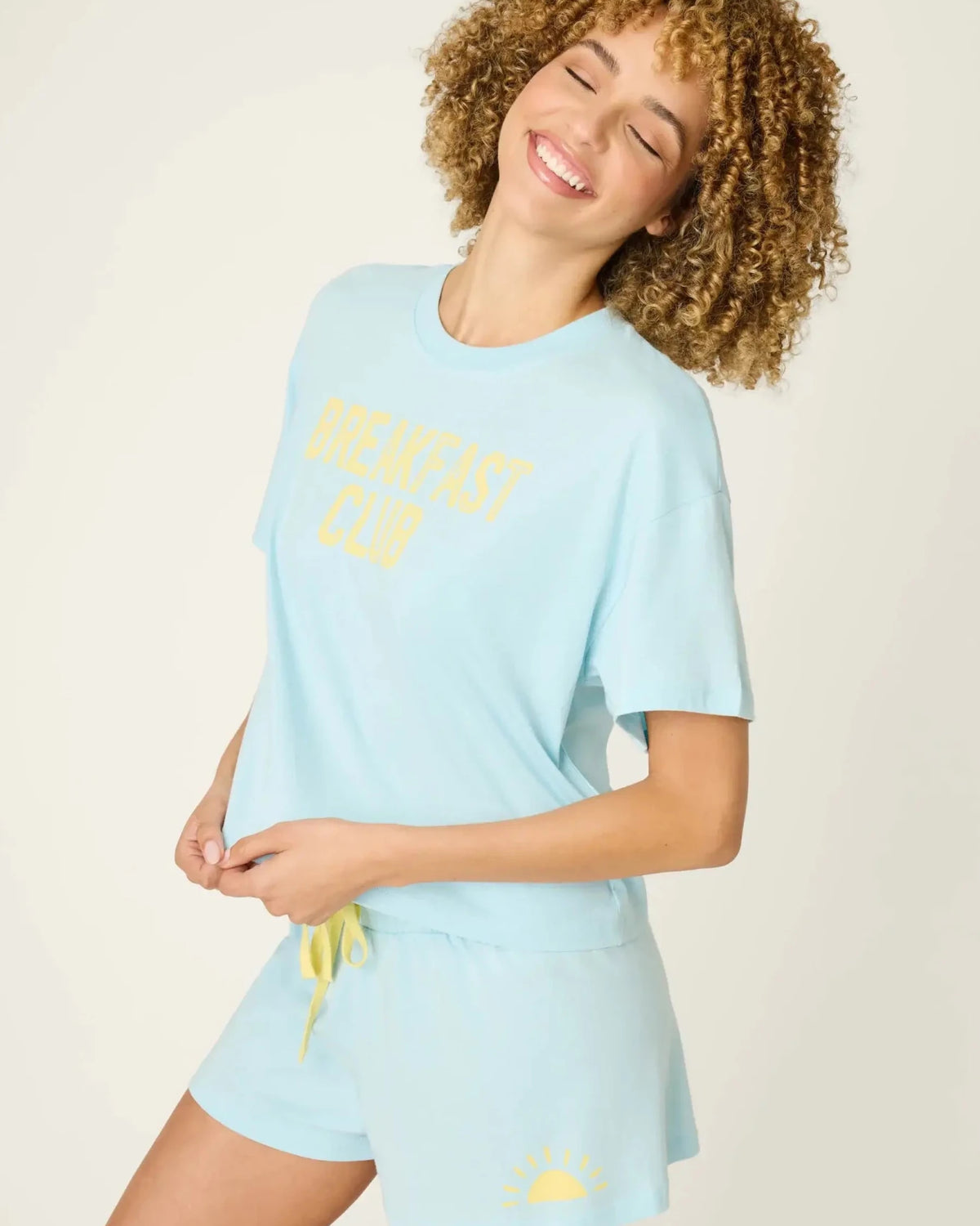 PJ SALVAGE Graphic Print Softee Tee & Short Lounge Set in "Breakfast Club" graphic tee shirt in light blue. Model stands against a light background in a lifestyle profile shot