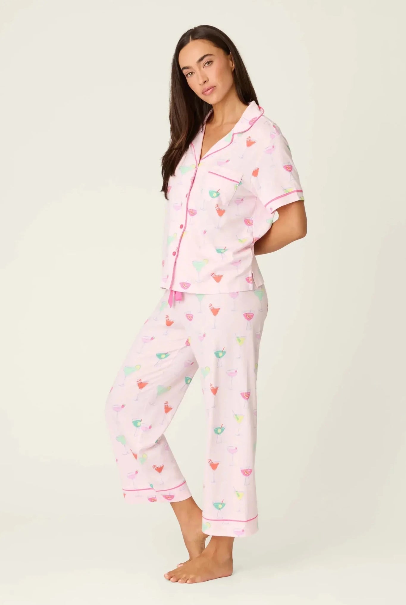 PJ SALVAGE Whimsy Cropped PJ Set in Light Pink Sip Happens print showing cocktail glasses in various colours. Model stands wearing the set against a light background showing the full length in a side profile