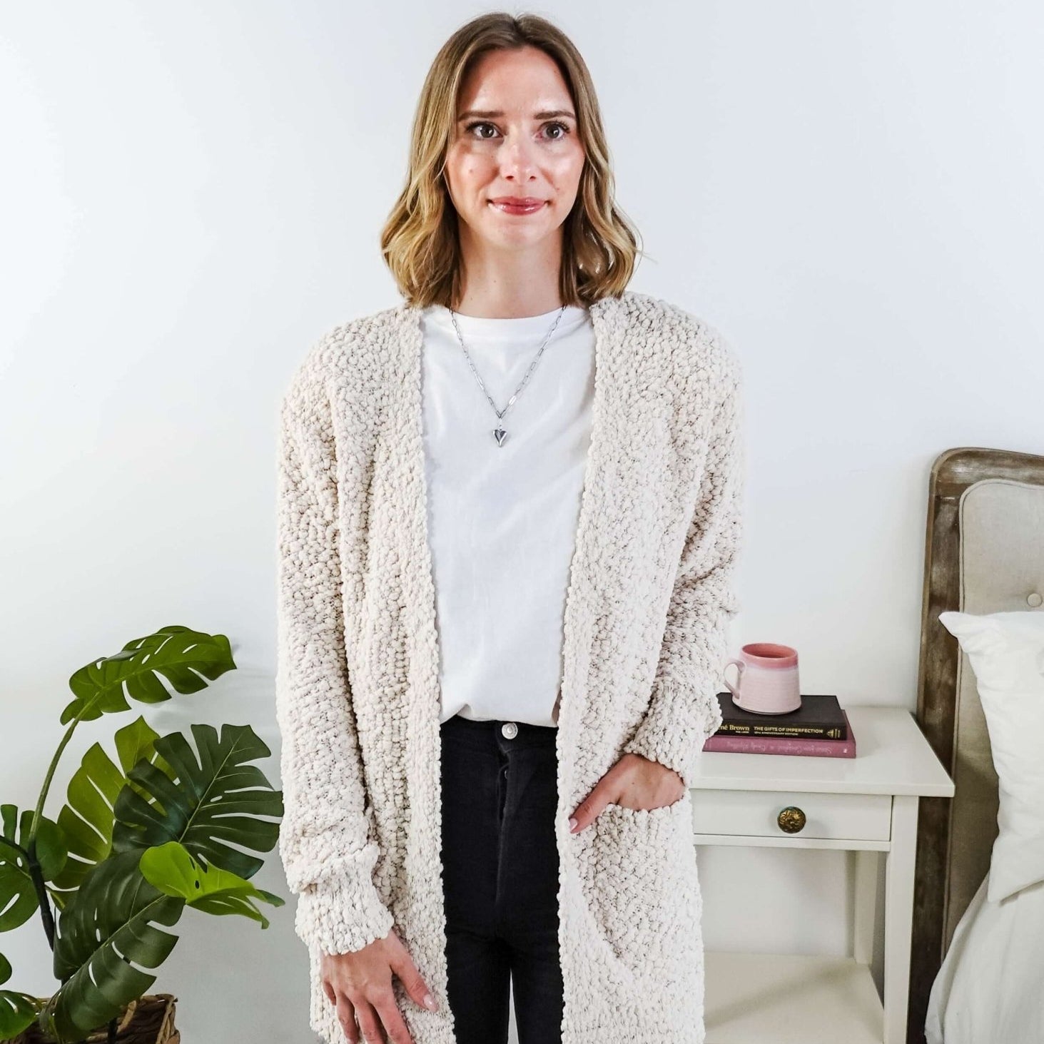 Popcorn Texture Open Summer Cardigan in sand beige, worn by Woman wearing a beige cardigan in a bedroom setting with a white tee and black jeans