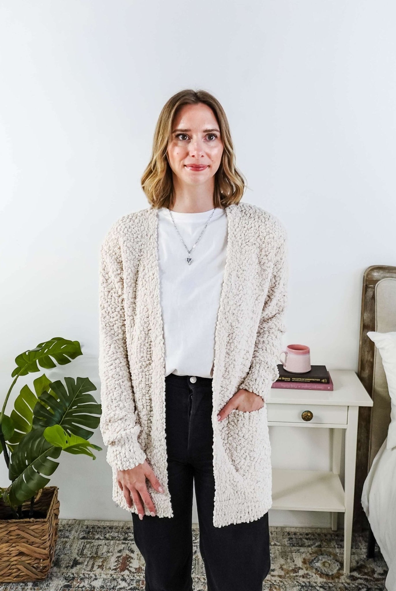 Popcorn Texture Open Summer Cardigan in sand beige, worn by Woman wearing a beige cardigan in a bedroom setting with a white tee and black jeans