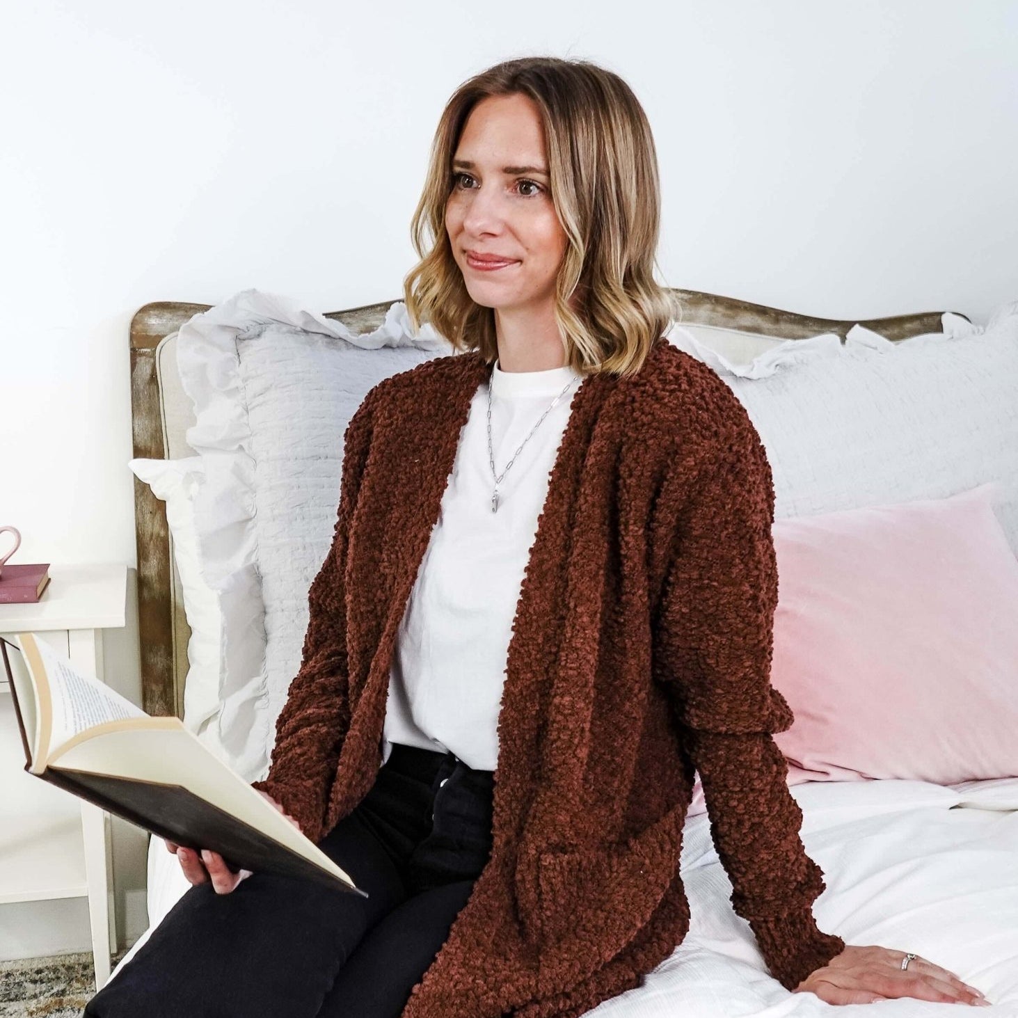 Popcorn Texture Open Summer Cardigan model sits on a bed wearing the rich earthy chocolate brown textured sweater