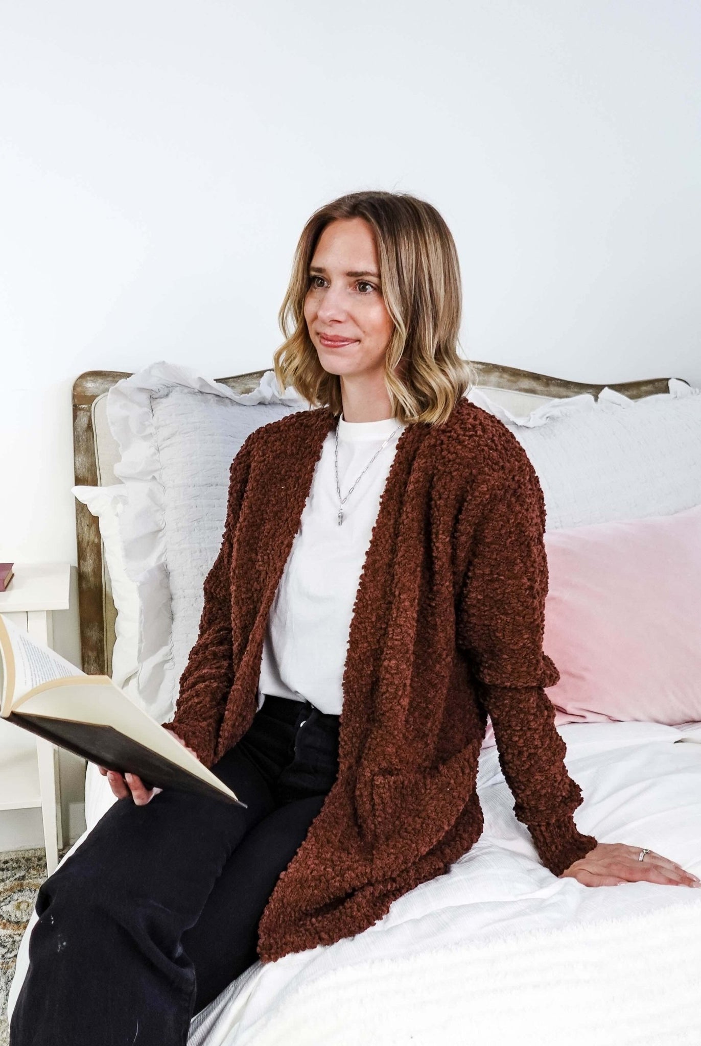 Popcorn Texture Open Summer Cardigan model sits on a bed wearing the rich earthy chocolate brown textured sweater