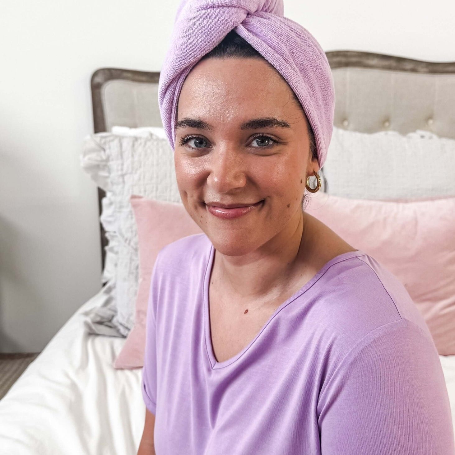Woman wearing the Remove It Quick Dry Microfiber Hair Towel Wrap in lavender color, smiling on a bed.