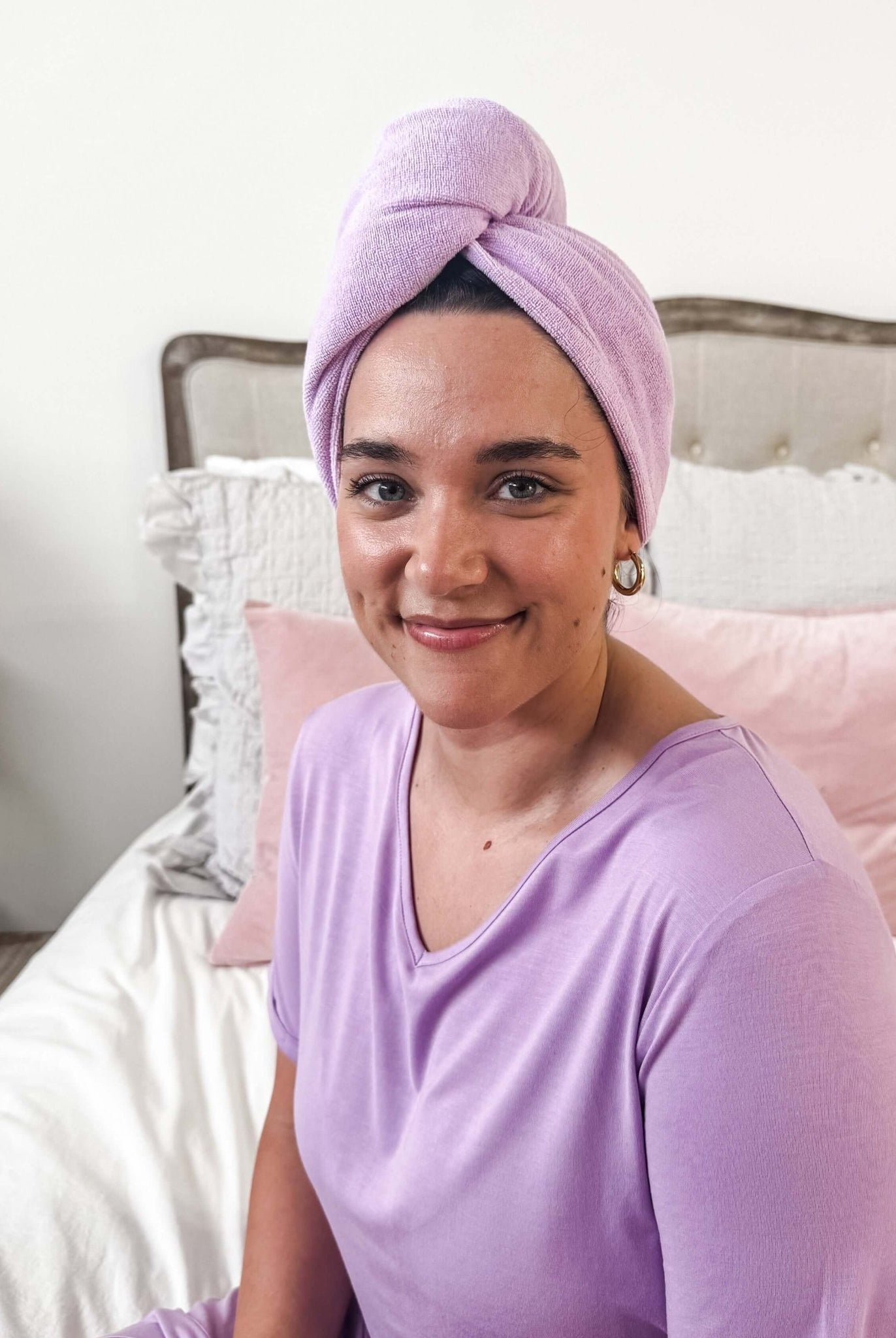 Woman wearing the Remove It Quick Dry Microfiber Hair Towel Wrap in lavender color, smiling on a bed.