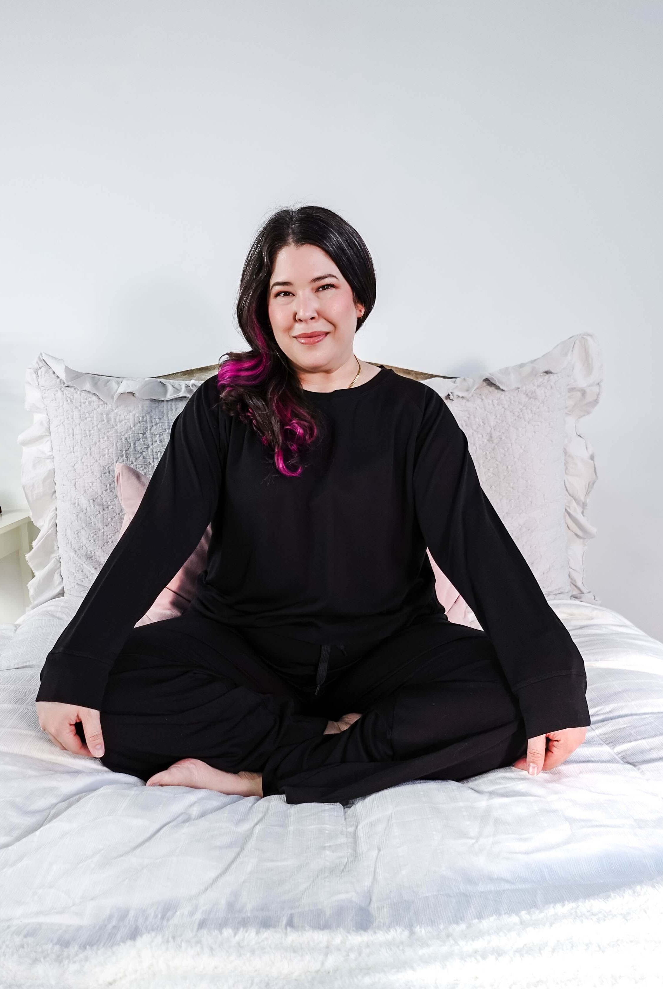 Black Long Sleeve Raw Edge Straight Pant Cloud Lounge Set worn by a woman sitting cross-legged on a bed.
