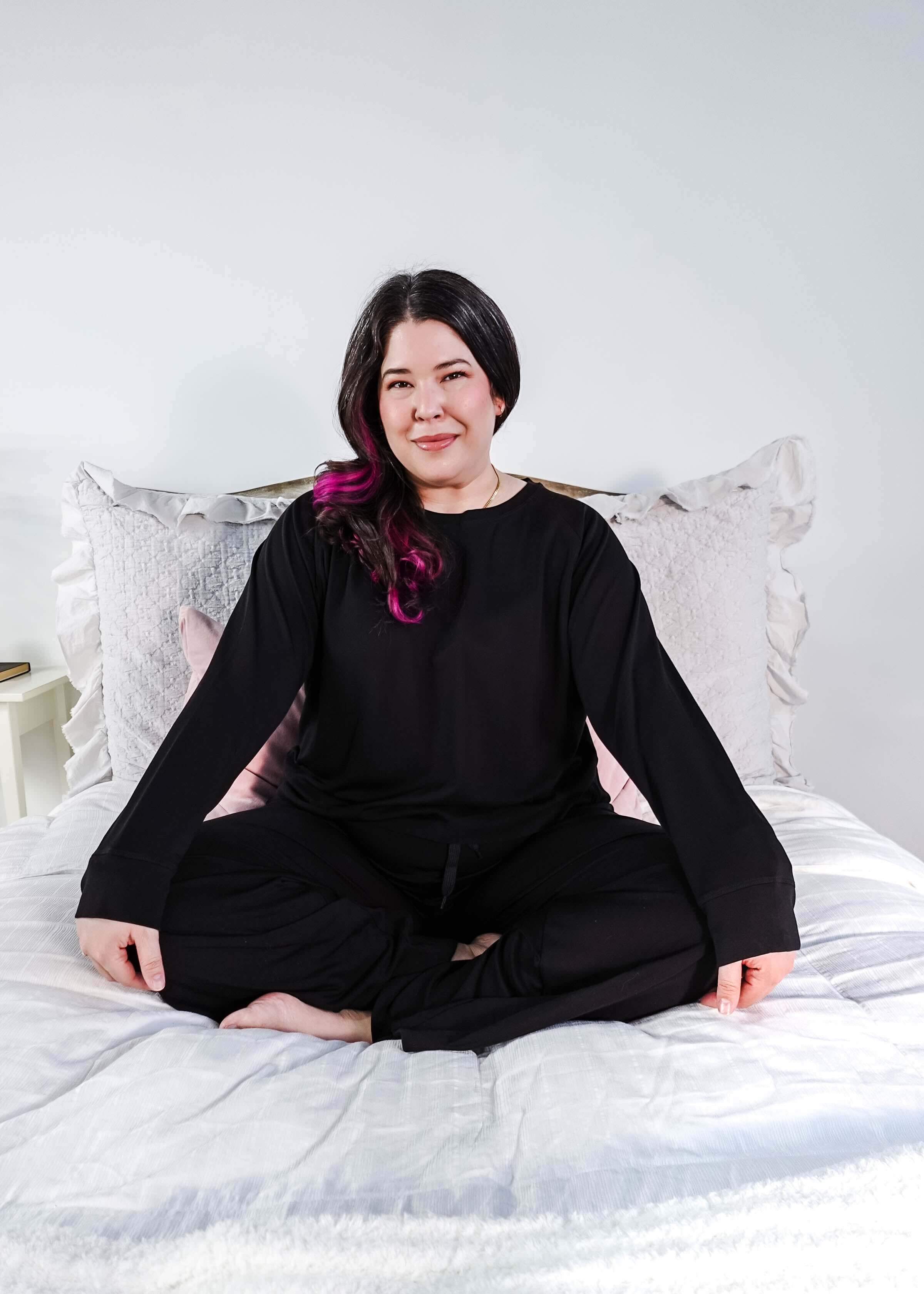 Black Long Sleeve Raw Edge Straight Pant Cloud Lounge Set worn by a woman sitting cross-legged on a bed.