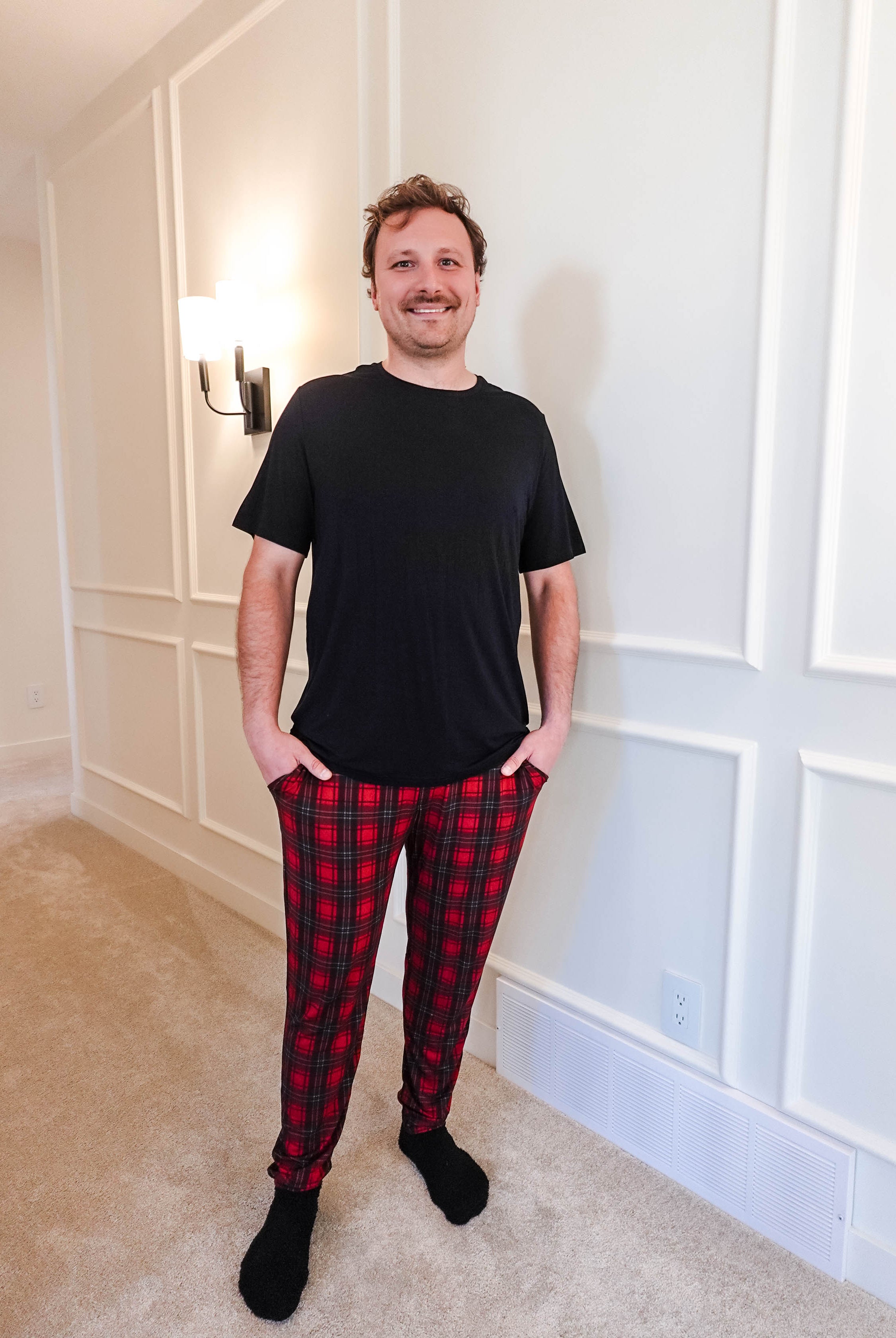 A man wearing a black shirt and Red Plaid Unisex Bamboo Jogger from Bob's Sleepwear Co. standing in a well-lit room.