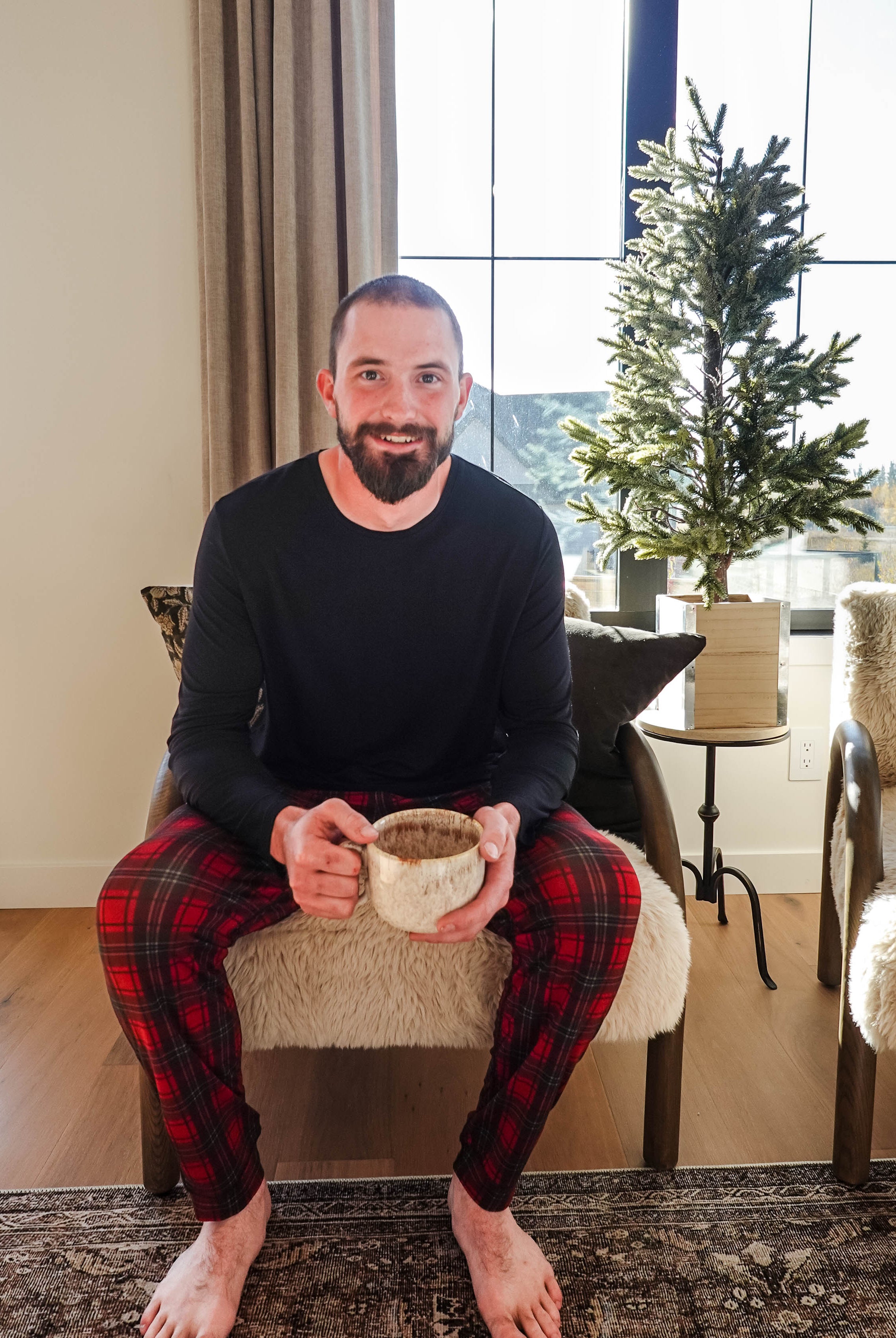 Man sitting in a chair wearing Red Plaid Unisex Bamboo Jogger, holding a mug, in a cozy living room setting.