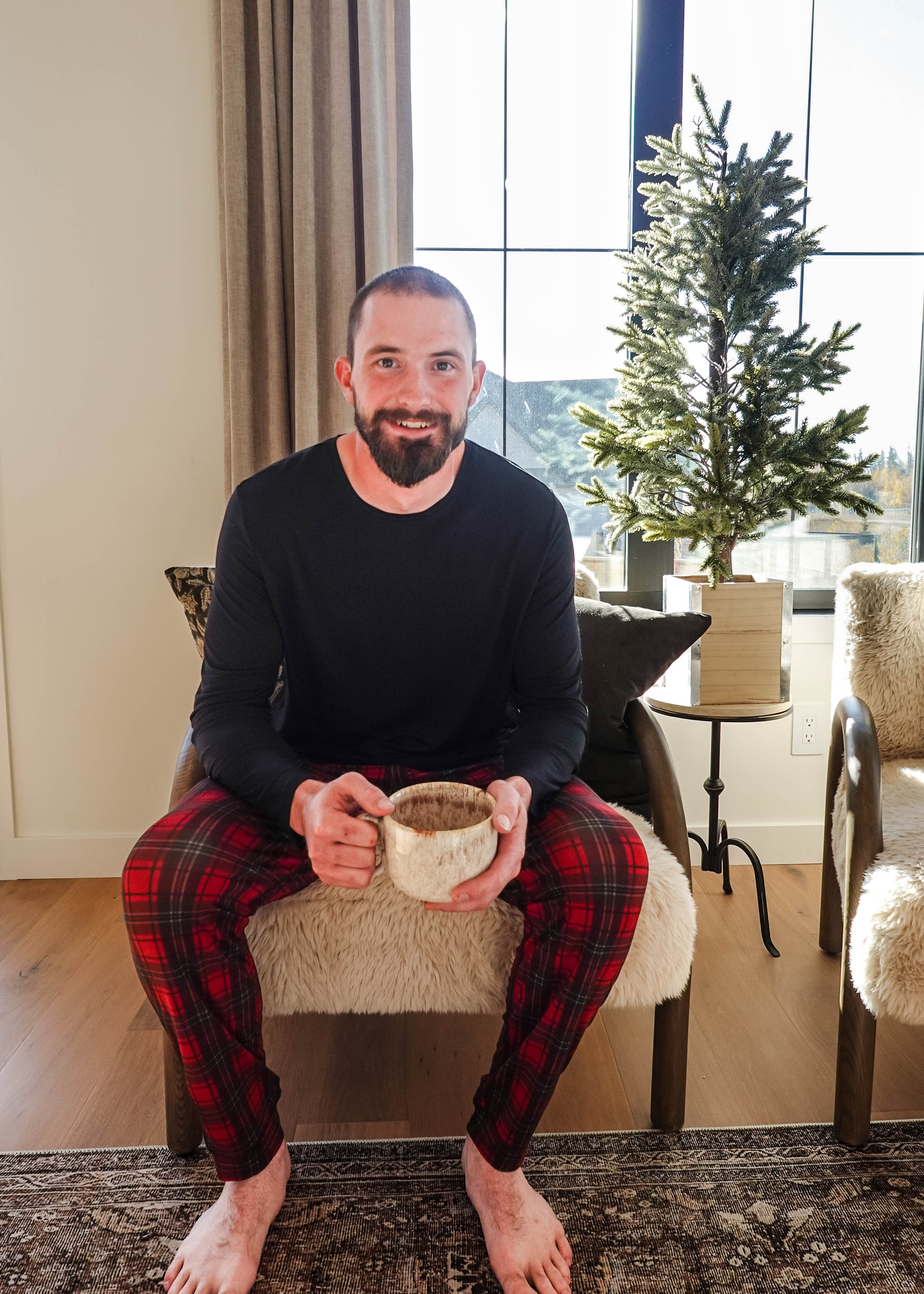 Man sitting in a chair wearing Red Plaid Unisex Bamboo Jogger, holding a mug, in a cozy living room setting.