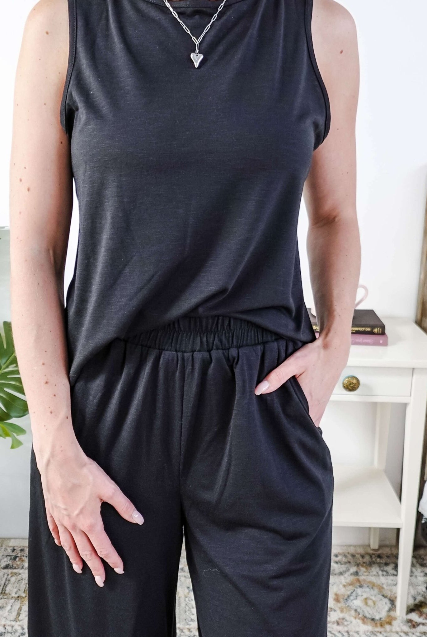 Woman wearing a sleepwear set with a black sleeveless top and pants in a home setting. With elastic waistband.