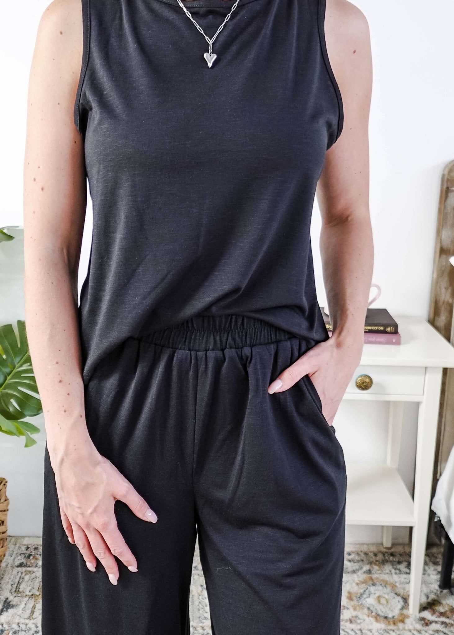 Woman wearing a sleepwear set with a black sleeveless top and pants in a home setting. With elastic waistband.
