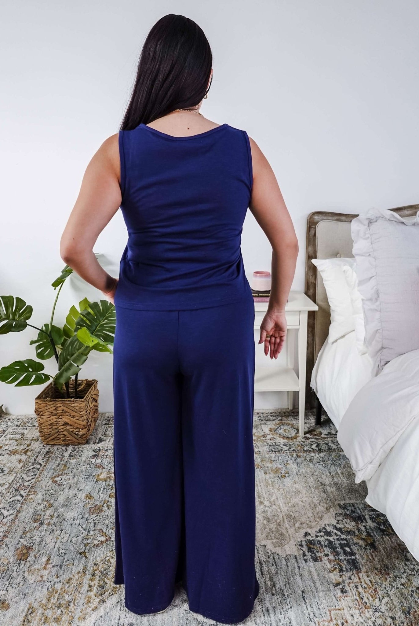 the back of a woman wearing a sleepwear set with a navy sleeveless top and pants in a home setting.