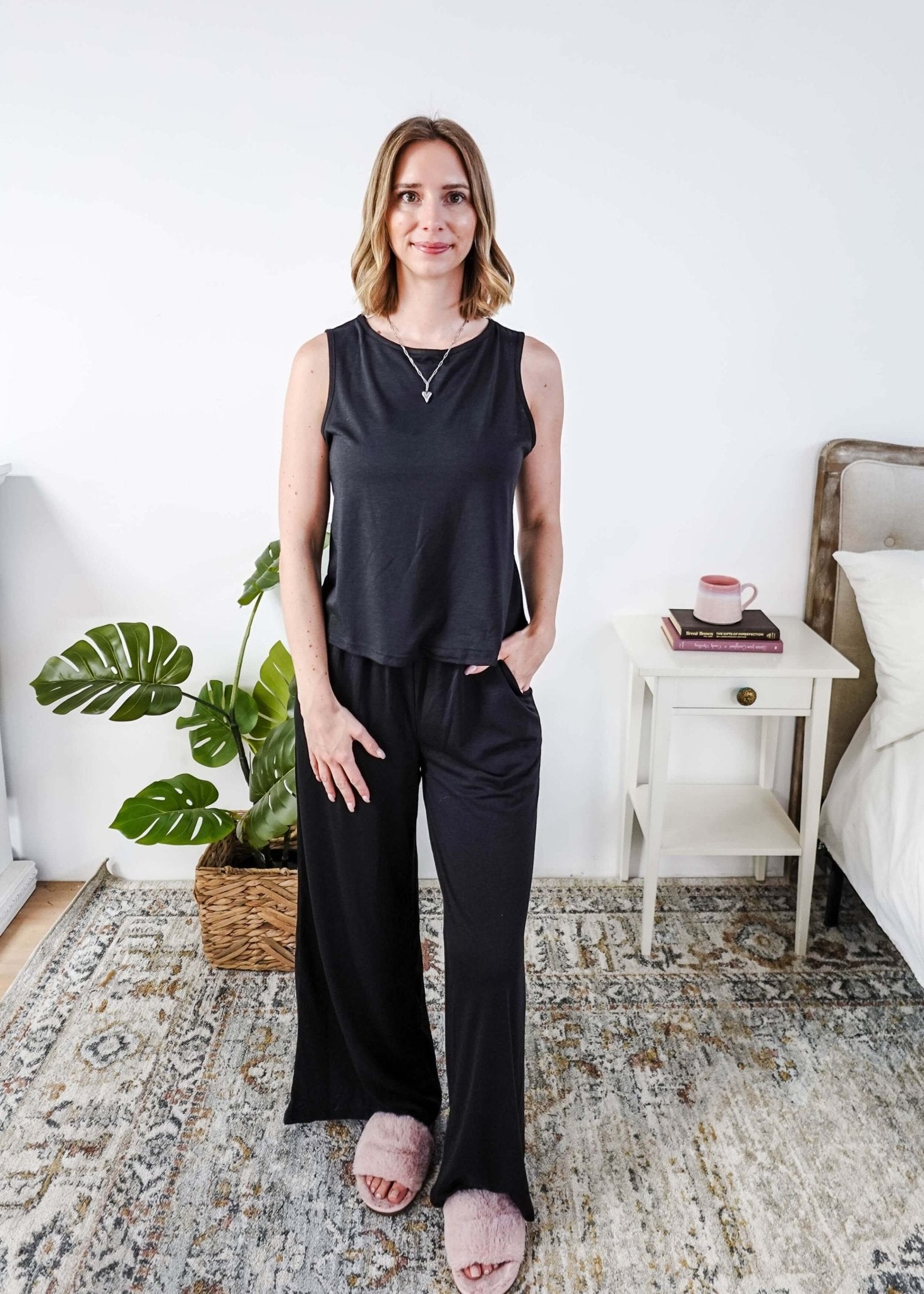 Woman wearing a sleepwear set with a black sleeveless top and pants in a home setting.