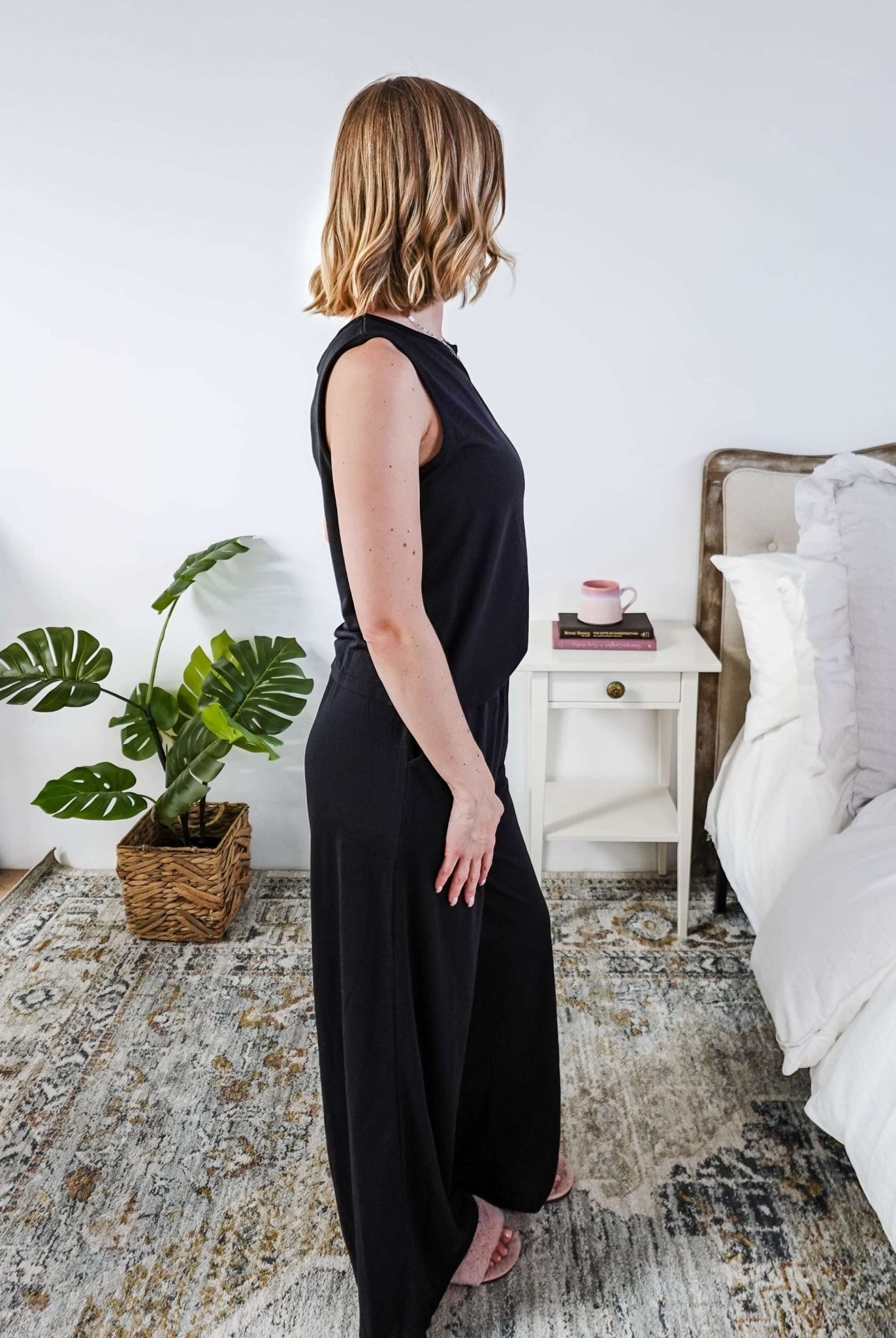 Woman wearing a sleepwear set with a black sleeveless top and pants in a home setting.
