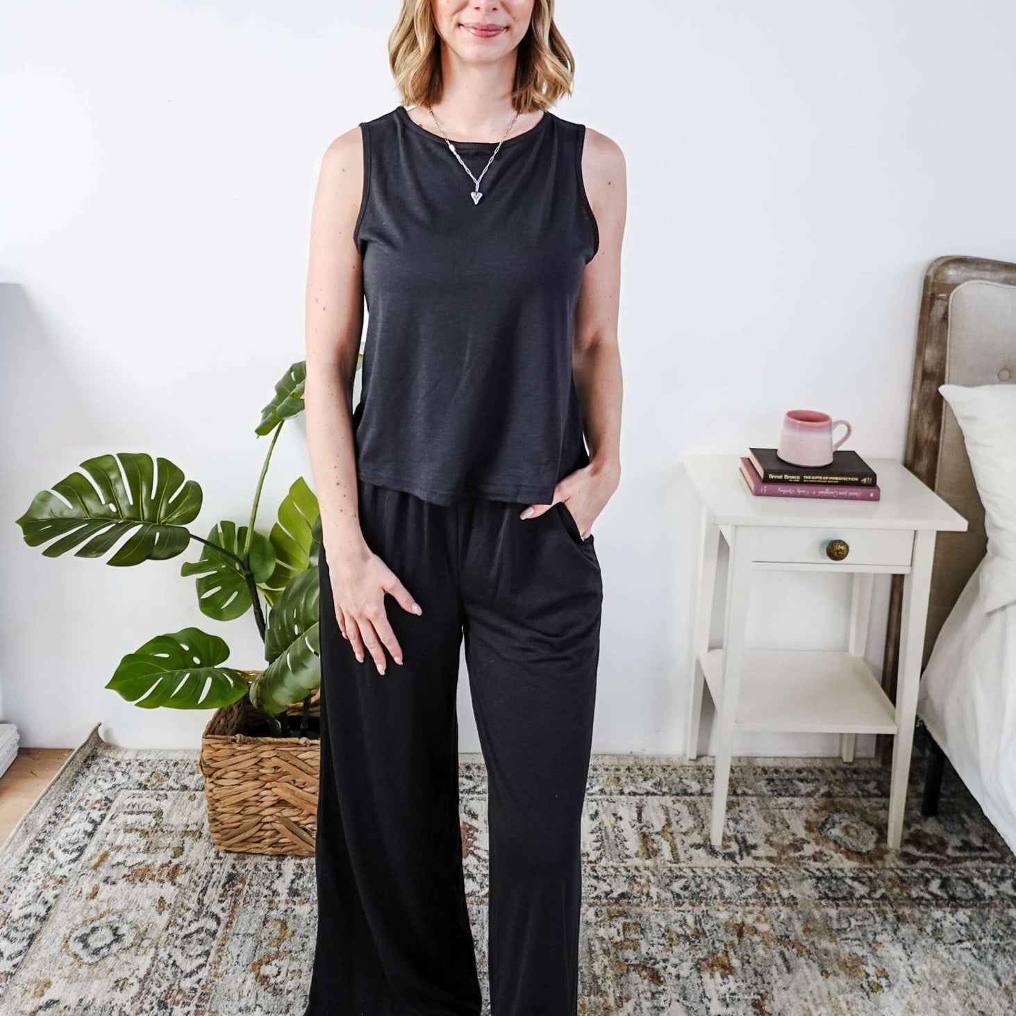 Woman wearing a sleepwear set with a black sleeveless top and pants in a home setting.