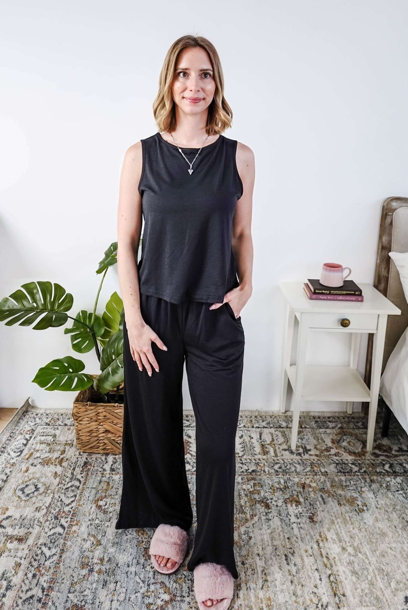 Woman wearing a sleepwear set with a black sleeveless top and pants in a home setting.