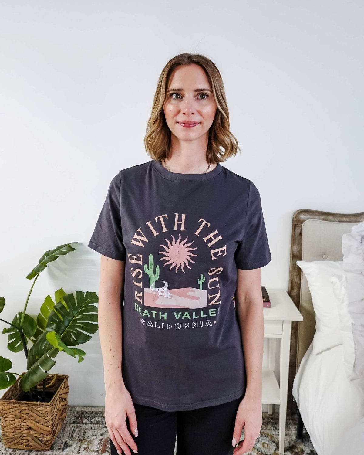 women wearing a dark grey graphic t-shirt with the saying rise with the sun death valley california